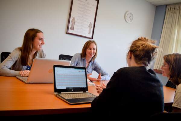 four students discussing at a table with laptops