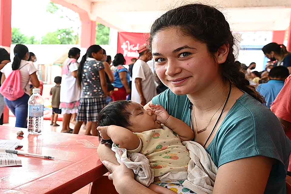 A student holds a young child while on a mission trip