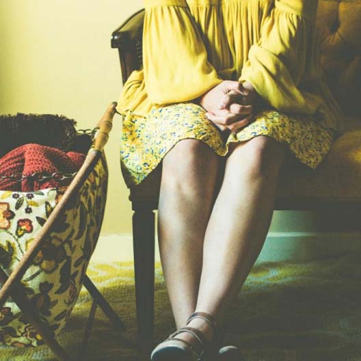 A photo of a girl dressed in yellow sitting next to a container of knitted articles of clothing